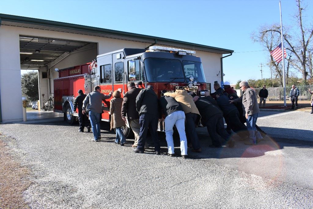 Photo of dignitaries and firefighters pushing the new fire truck into the station